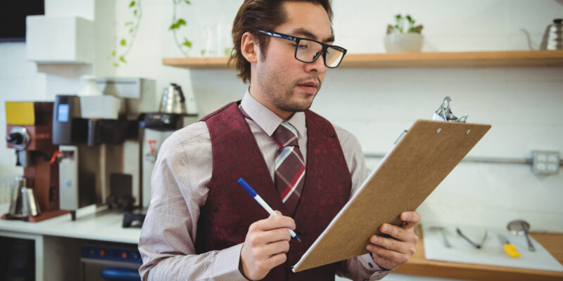 Man writing with pen on clipboard in coffee shop CMMC Compliance Checklist